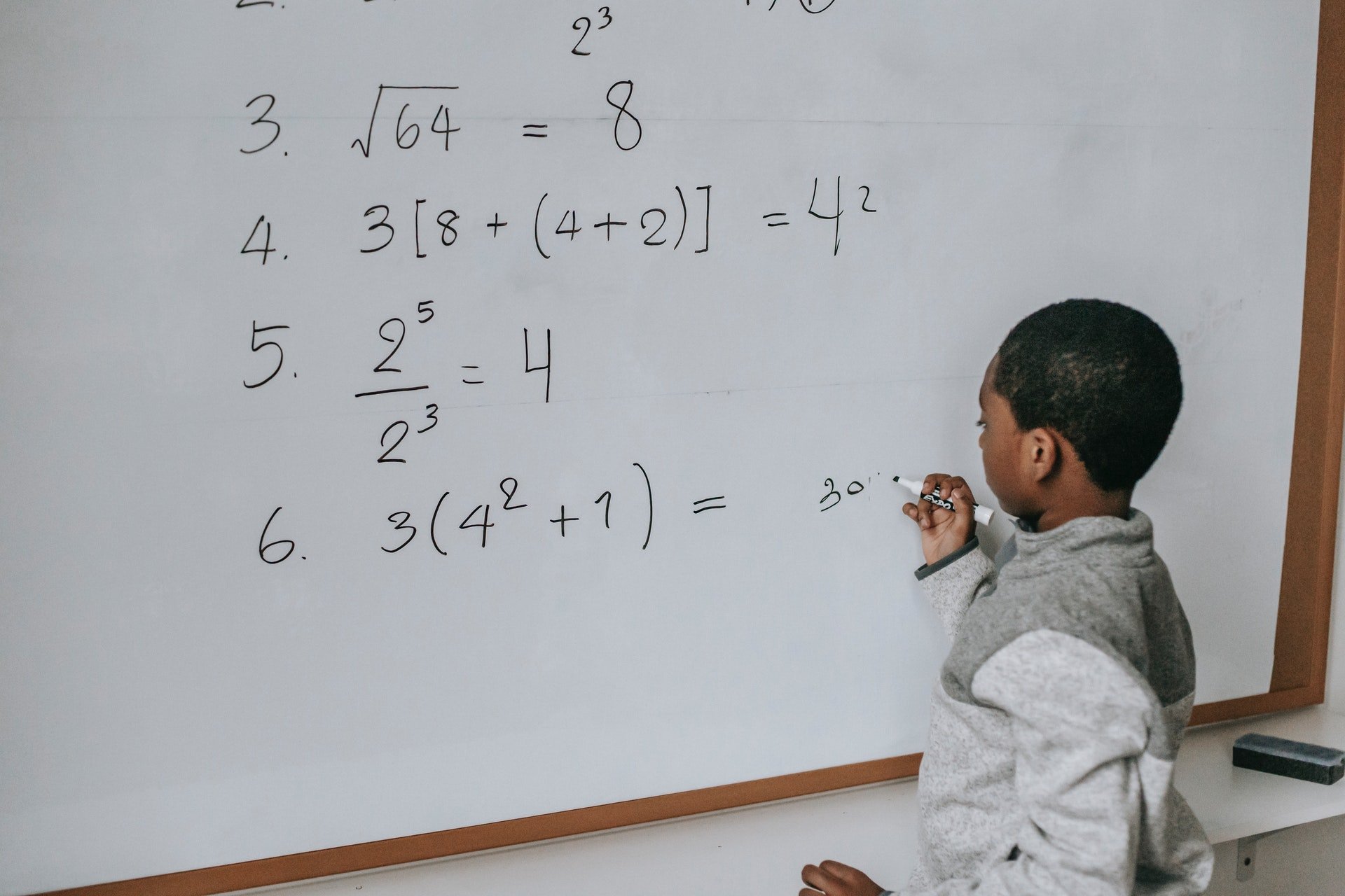 Elementary student writing on white board doing math problems 