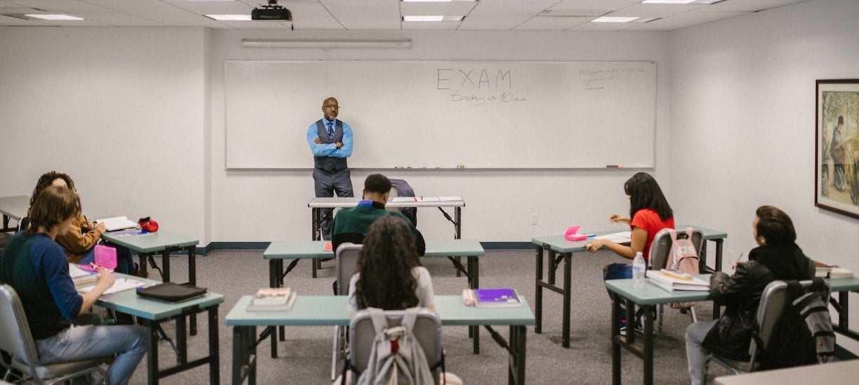 Students taking a test with a teacher at front the classroom